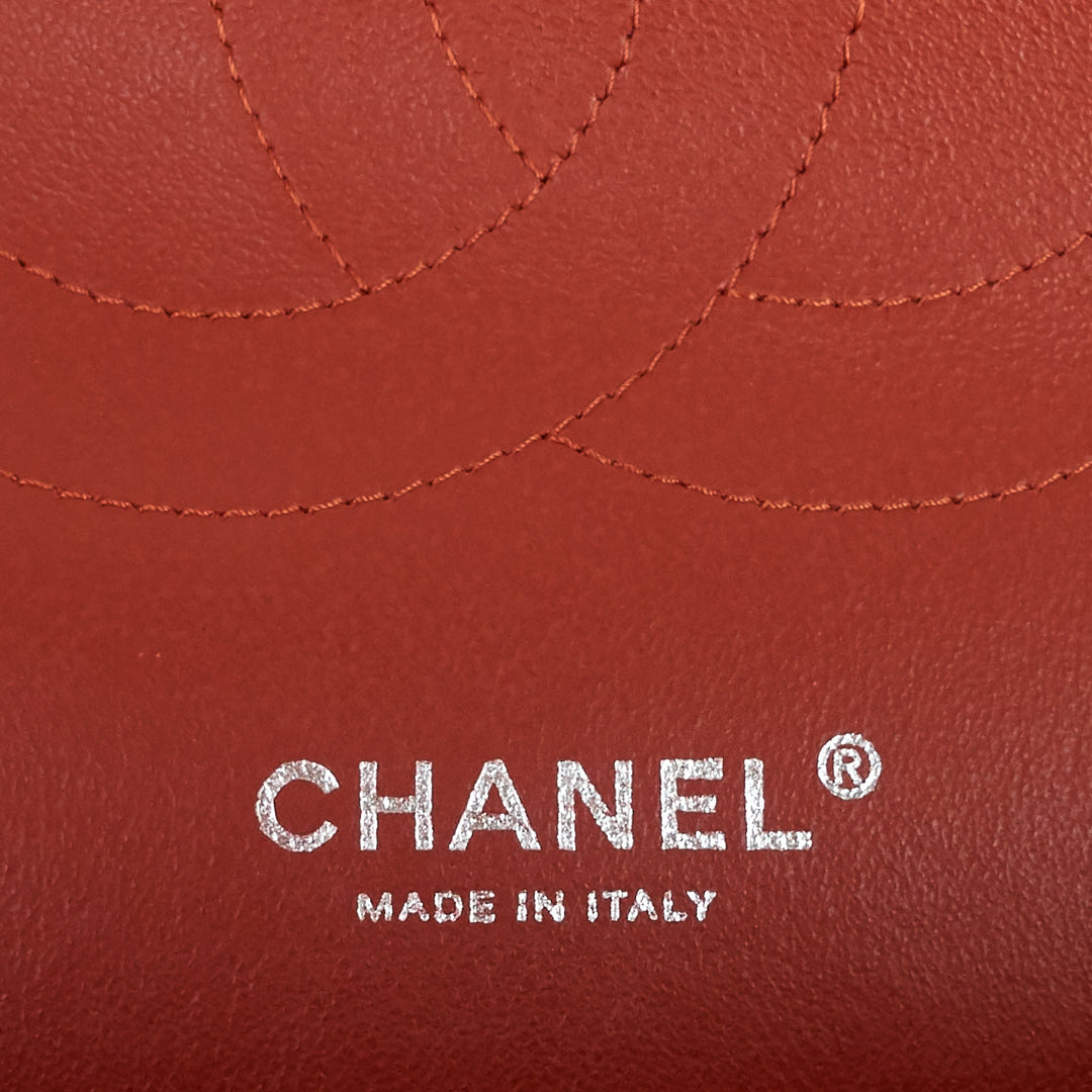 Close-up of a red leather product featuring the embossed Chanel logo and 'MADE IN ITALY' text, with curved stitching details.
