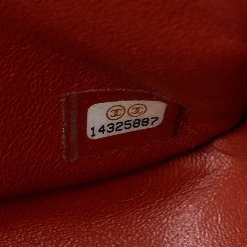 Close-up of a red textured leather item showing a sewn-on white label with two interlocking CC logos and the number 14325887.