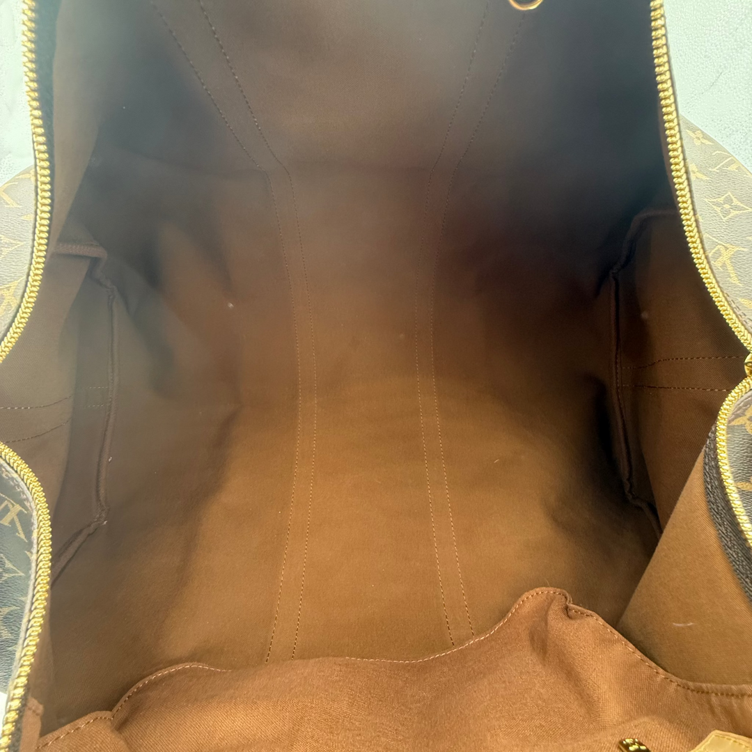 An empty view inside a Louis Vuitton monogram canvas bag, showing the brown suede-like interior lining, gold-tone zipper, and metal hardware.