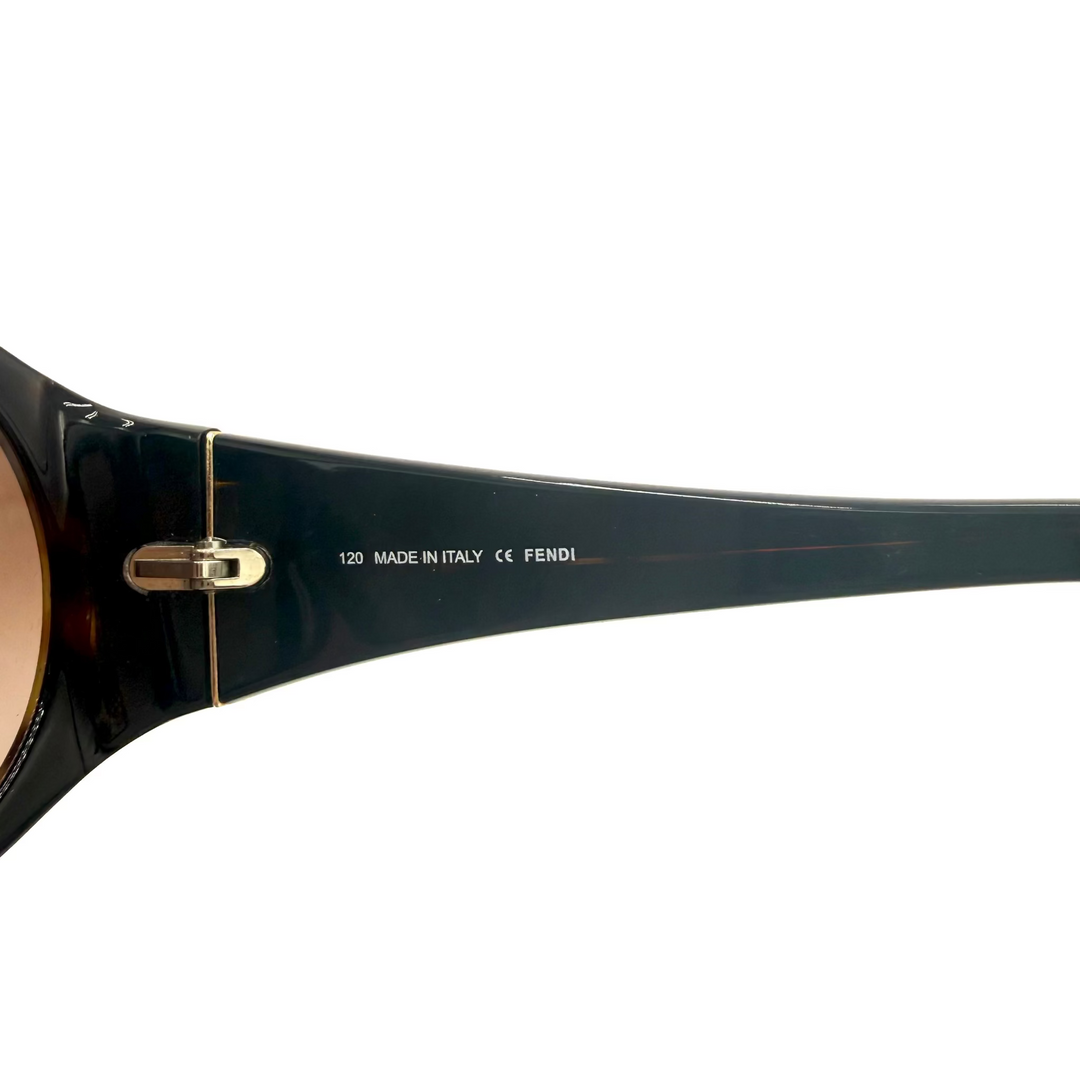Close-up of a Fendi sunglasses arm showing the brand name, 'MADE IN ITALY', and model number '120' in white text on a glossy dark tortoiseshell acetate, with a gold hinge and light brown lenses visible.