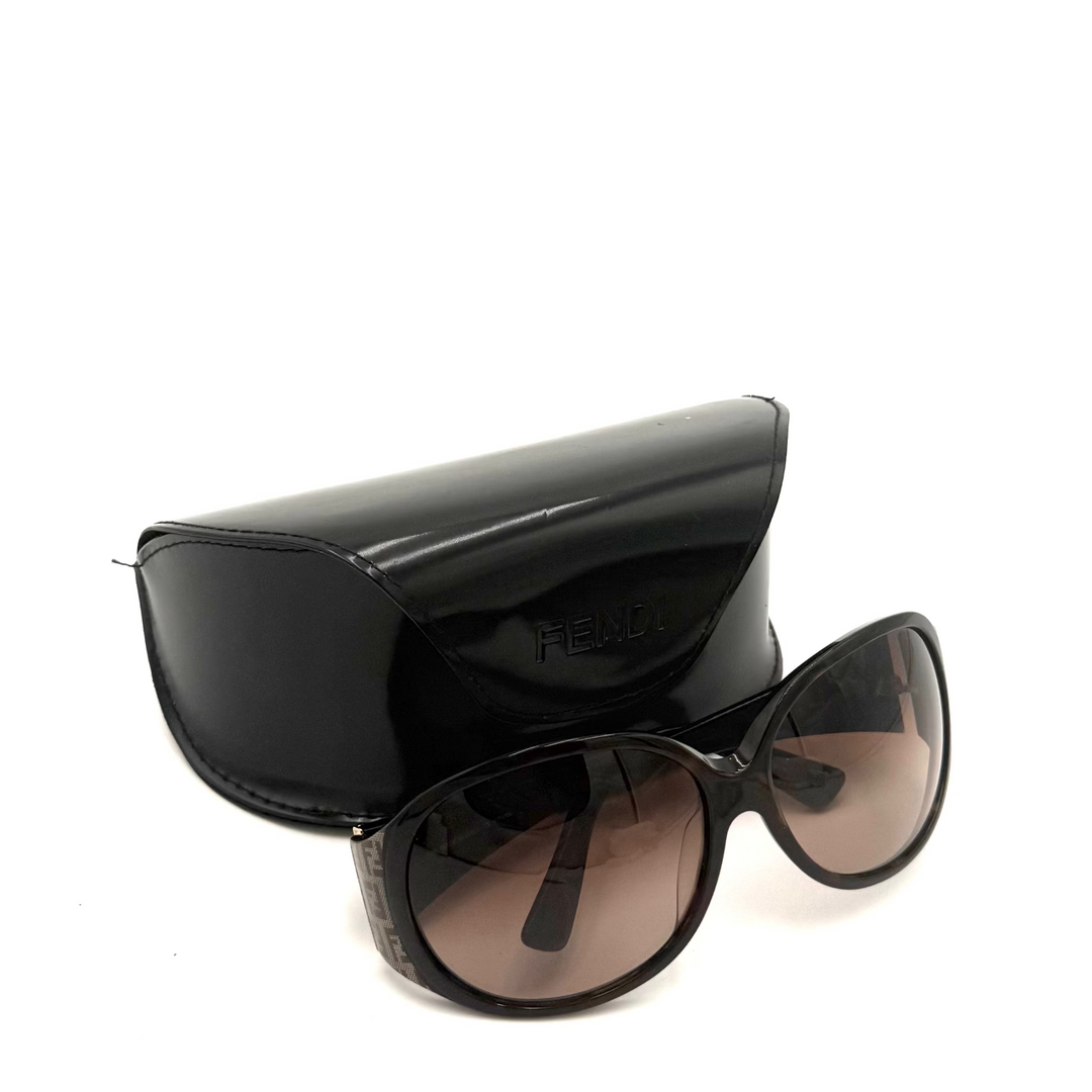 Fendi sunglasses with a glossy black frame and brown gradient lenses, shown with a matching black patent leather case on a white background.