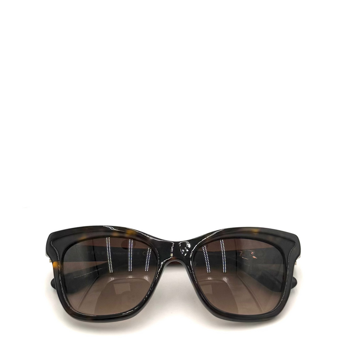 A pair of oversized square sunglasses with a glossy black acetate frame, featuring a subtle tortoiseshell pattern at the corners and dark brown gradient lenses.
