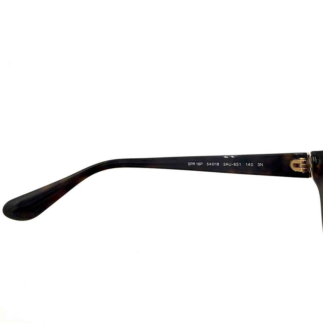 Close-up of tortoiseshell sunglasses with dark brown gradient lenses, showing the temple arm and part of the frame against a bright white background.