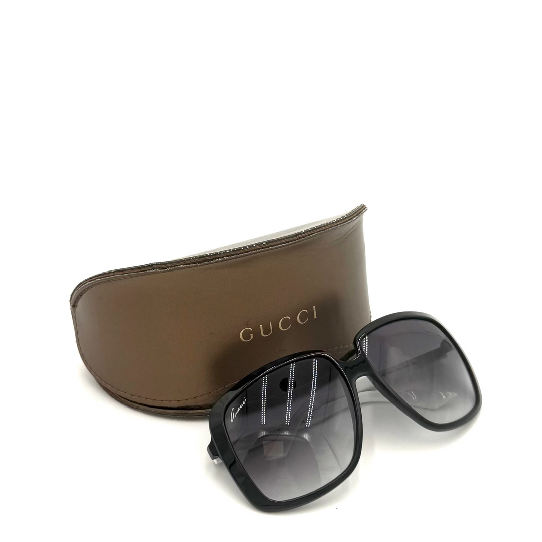 Gucci square sunglasses with a black frame and dark gray lenses, displayed in front of a brown leather case with the gold GUCCI logo on a white background.