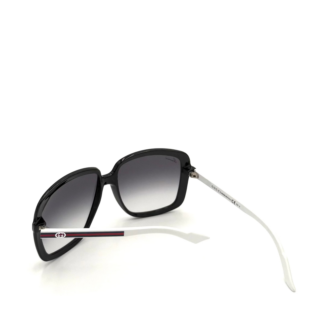 A pair of Gucci oversized sunglasses with a glossy black frame, gradient gray lenses, and white temples featuring the signature red and green Gucci stripe.
