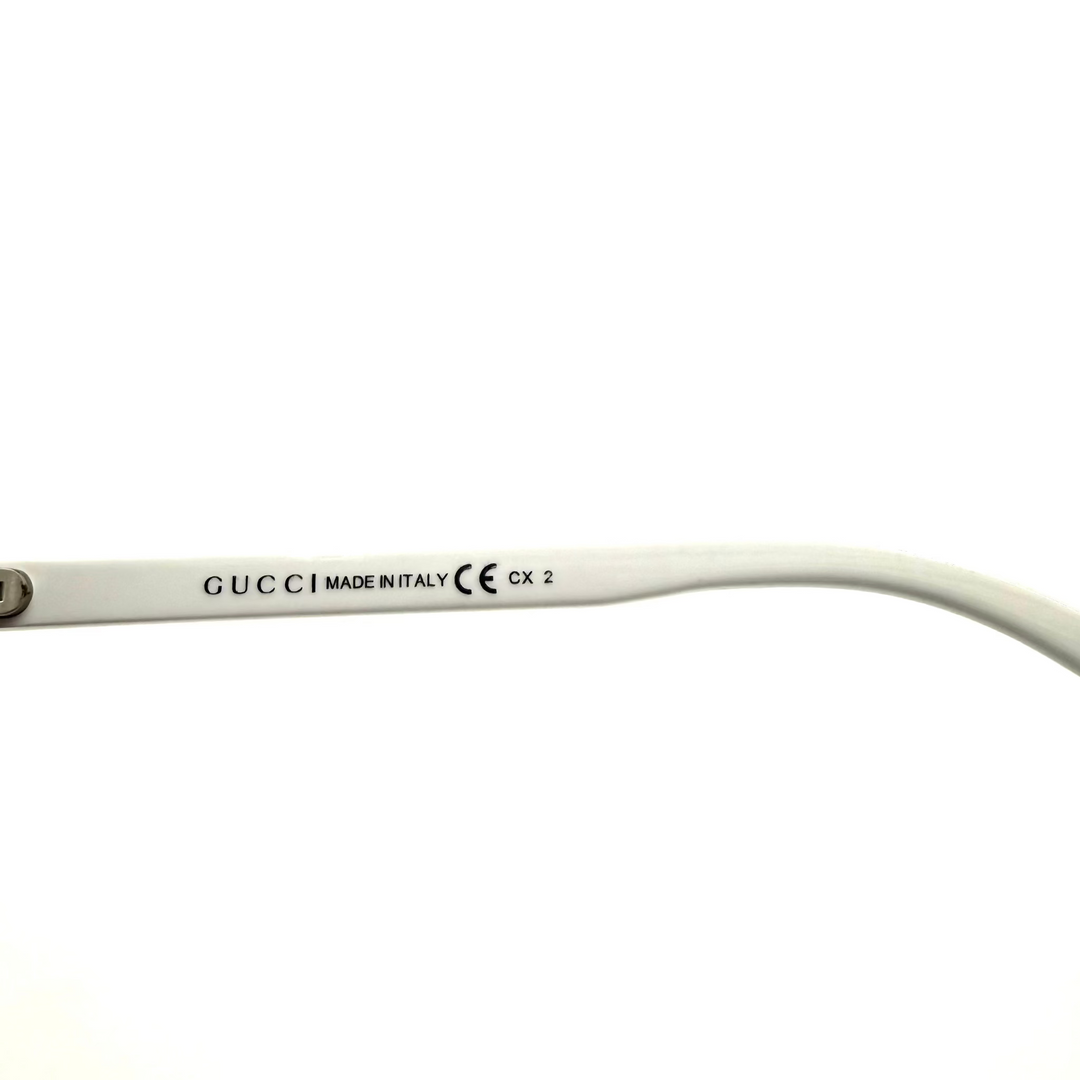 Close-up of a white Gucci sunglasses arm with black printed text including 'GUCCI MADE IN ITALY CE CX 2' on a white background.