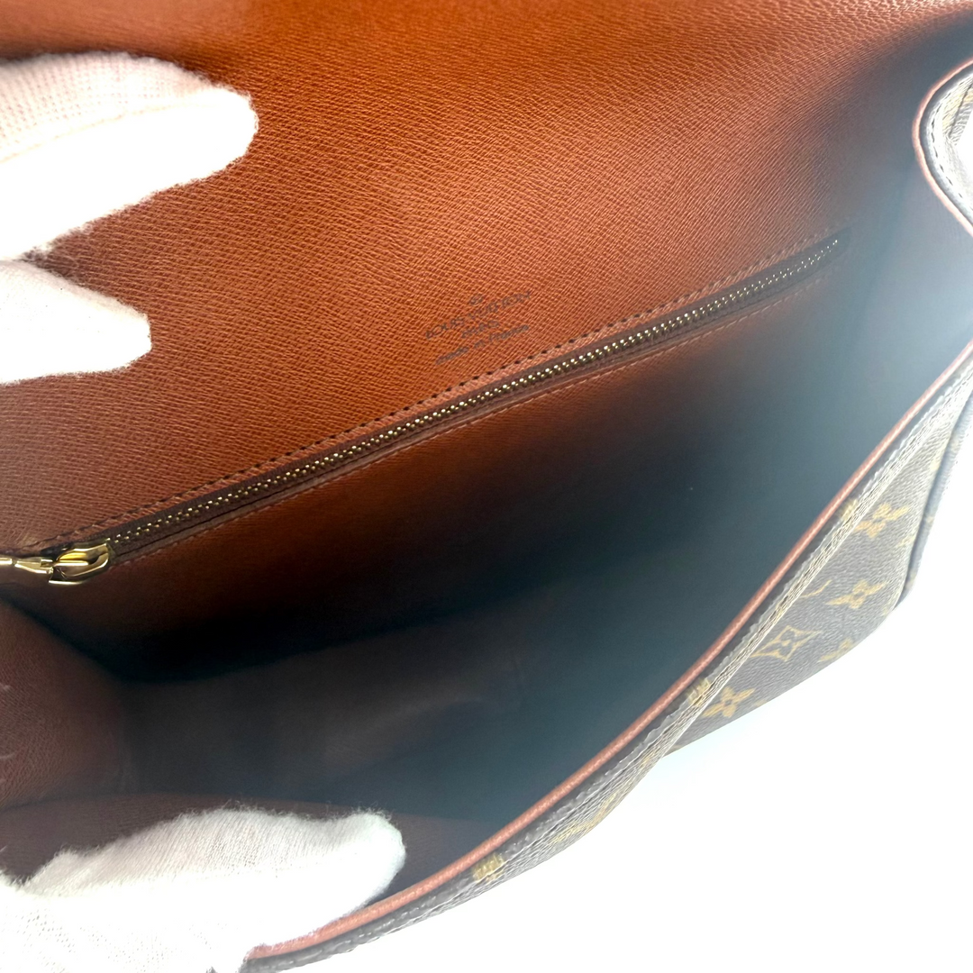 Close-up of the interior of a brown leather handbag, showing a zippered compartment and a small gold-tone zipper pull. A white-gloved hand is holding the bag open.