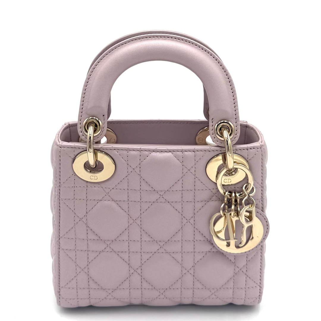 A light purple quilted leather top-handle handbag with gold-tone hardware and hanging CD charms, photographed on a clean white background.