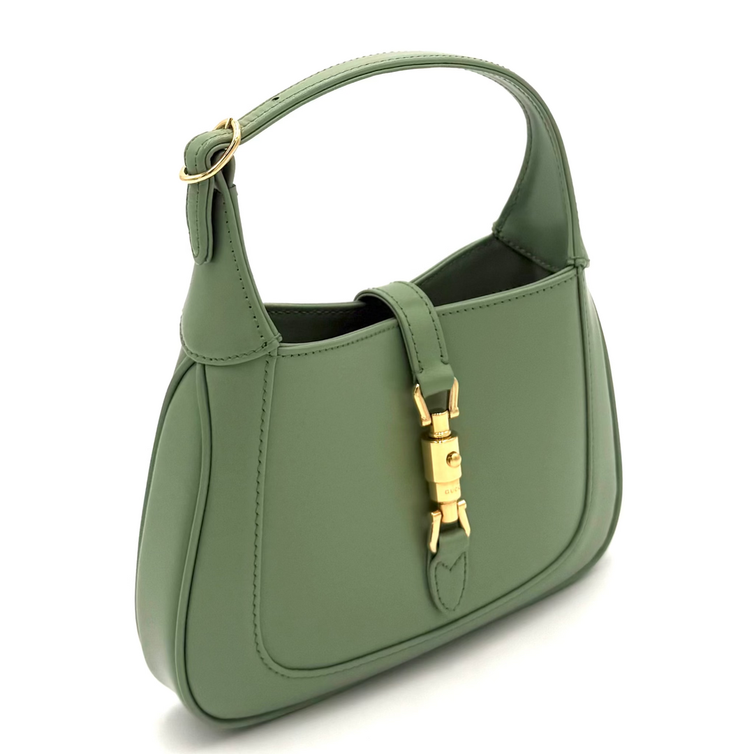 An olive green leather shoulder bag with gold-tone hardware, featuring a structured shape, a top handle, and a decorative front strap closure, shown on a plain white background.