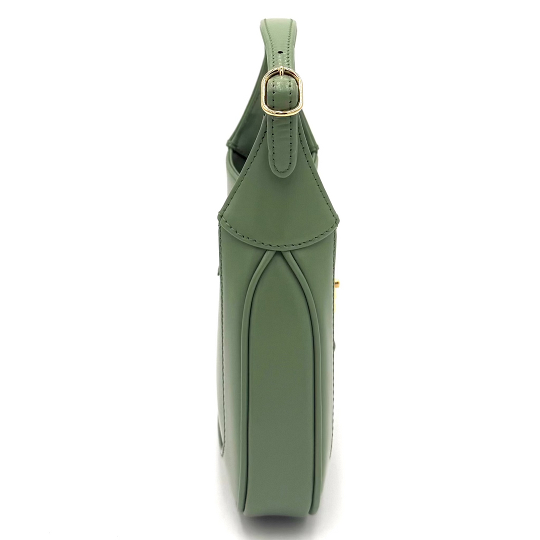 A sage green leather shoulder bag shown from a side profile view, featuring a gold-tone metal ring detail on the strap and a structured silhouette, set against a plain white background.