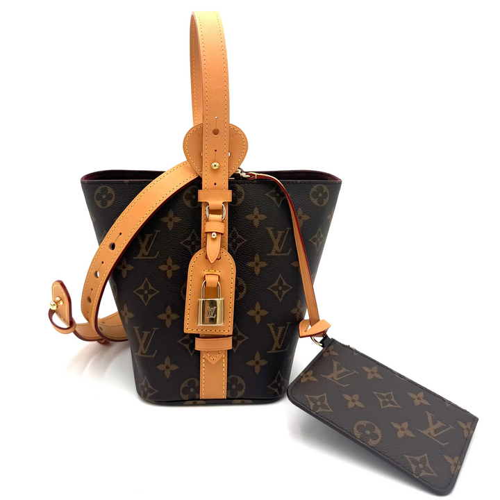 Louis Vuitton monogram canvas bucket bag with tan leather trim, a top handle, and a matching luggage tag on a white background.