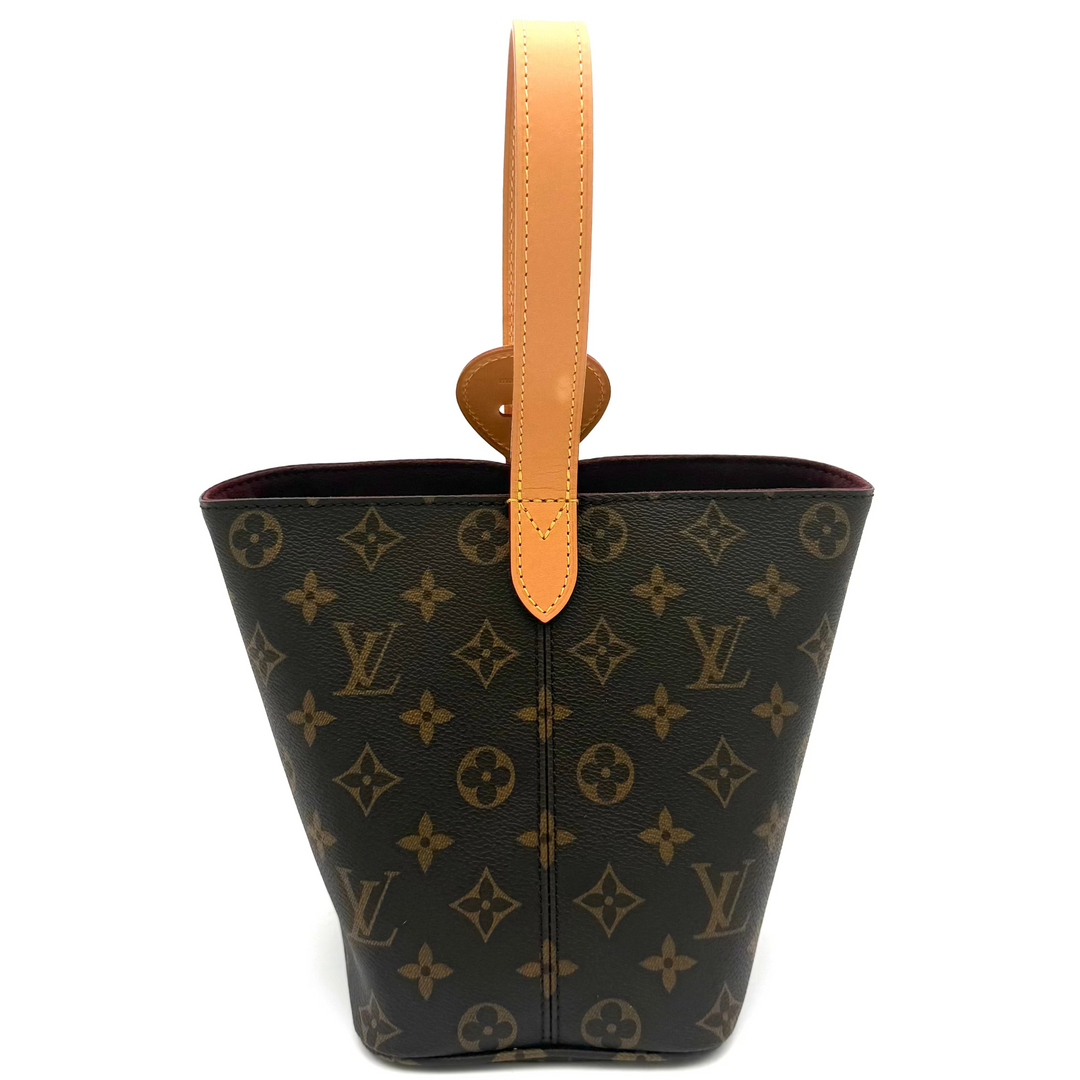 Louis Vuitton monogram canvas bucket bag with a tan leather top handle, shown against a plain white background.