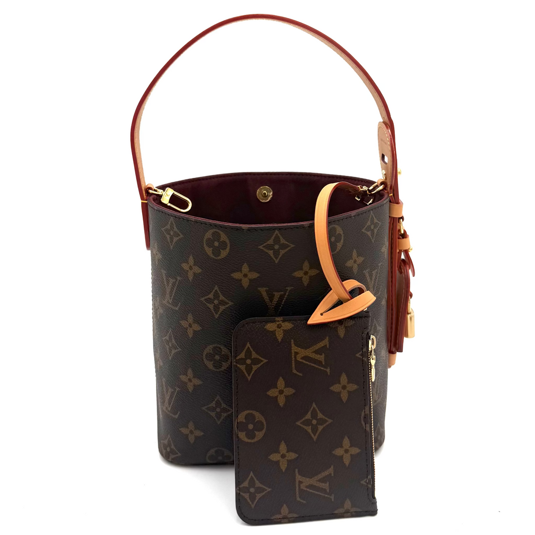 Louis Vuitton monogram canvas bucket bag with a top handle, gold-tone hardware, and a matching zippered pouch placed in front, photographed on a white background.