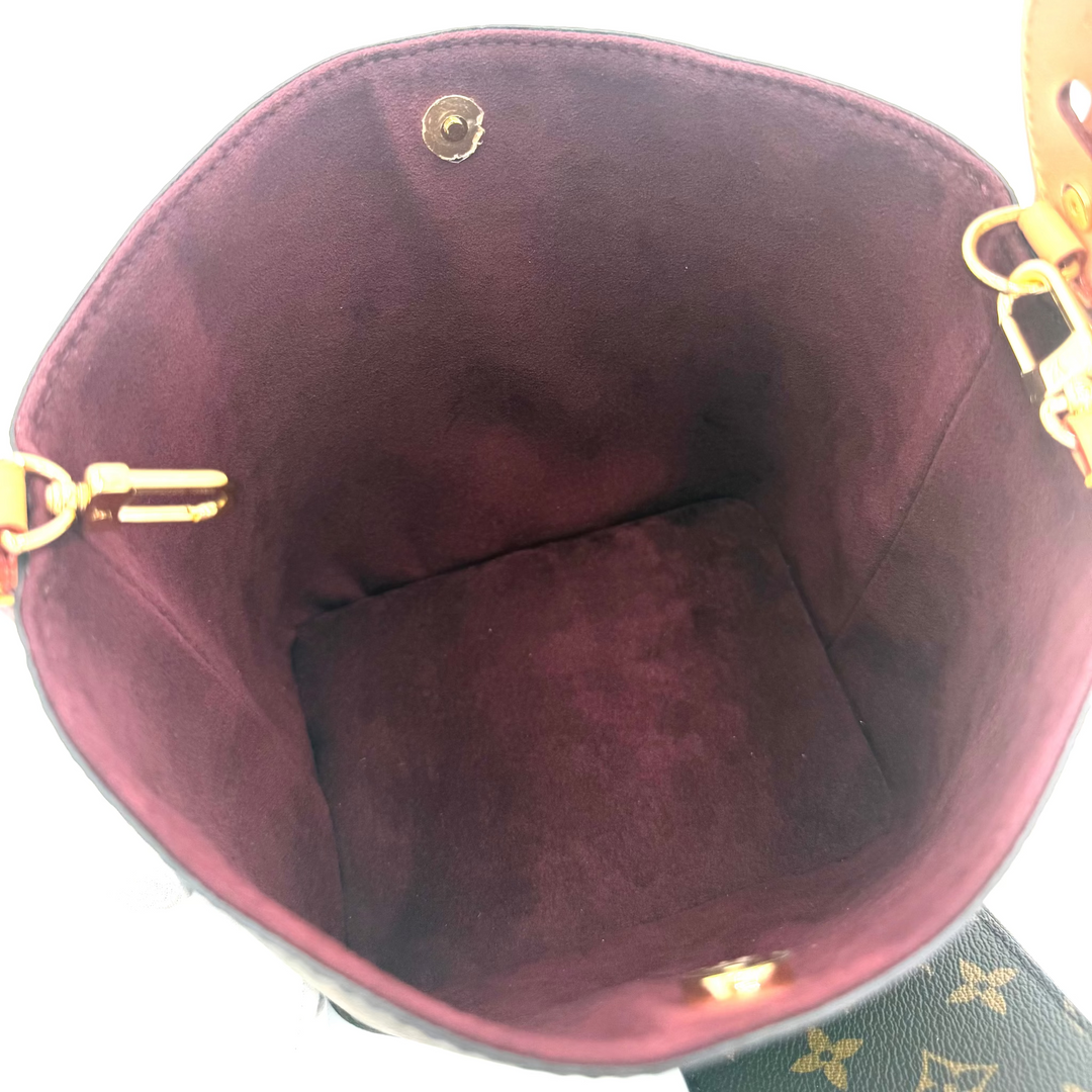 Top-down view of a Louis Vuitton bucket bag's interior, showing a deep burgundy suede lining with gold-tone hardware and a portion of the dark brown monogram canvas exterior visible at the bottom right.