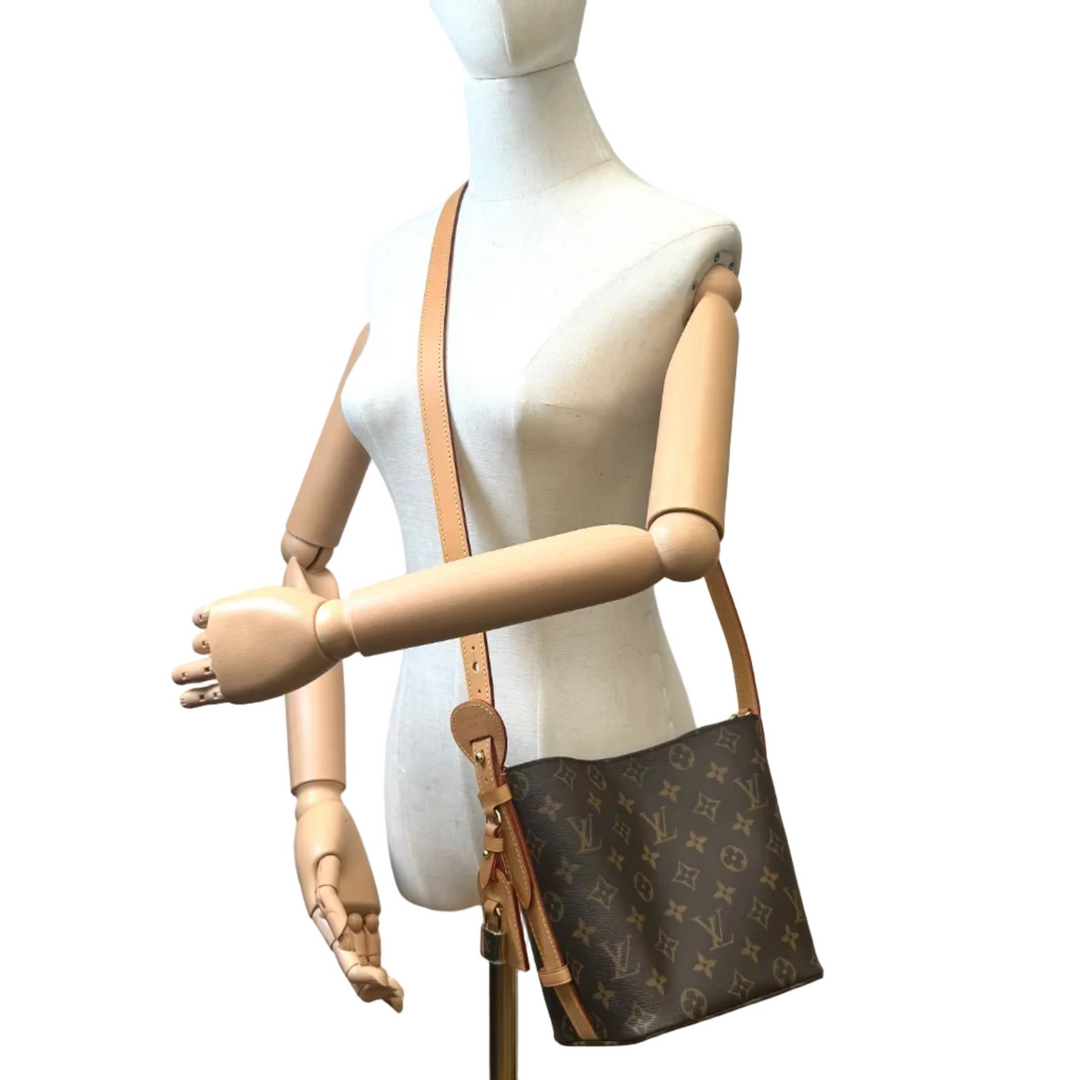 Louis Vuitton monogram canvas shoulder bag with tan leather strap, displayed on a white mannequin torso with wooden arms.