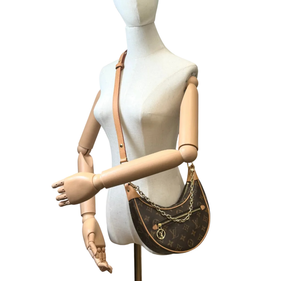 Louis Vuitton monogram shoulder bag in brown canvas with tan leather strap, displayed on a beige mannequin torso against a white background.