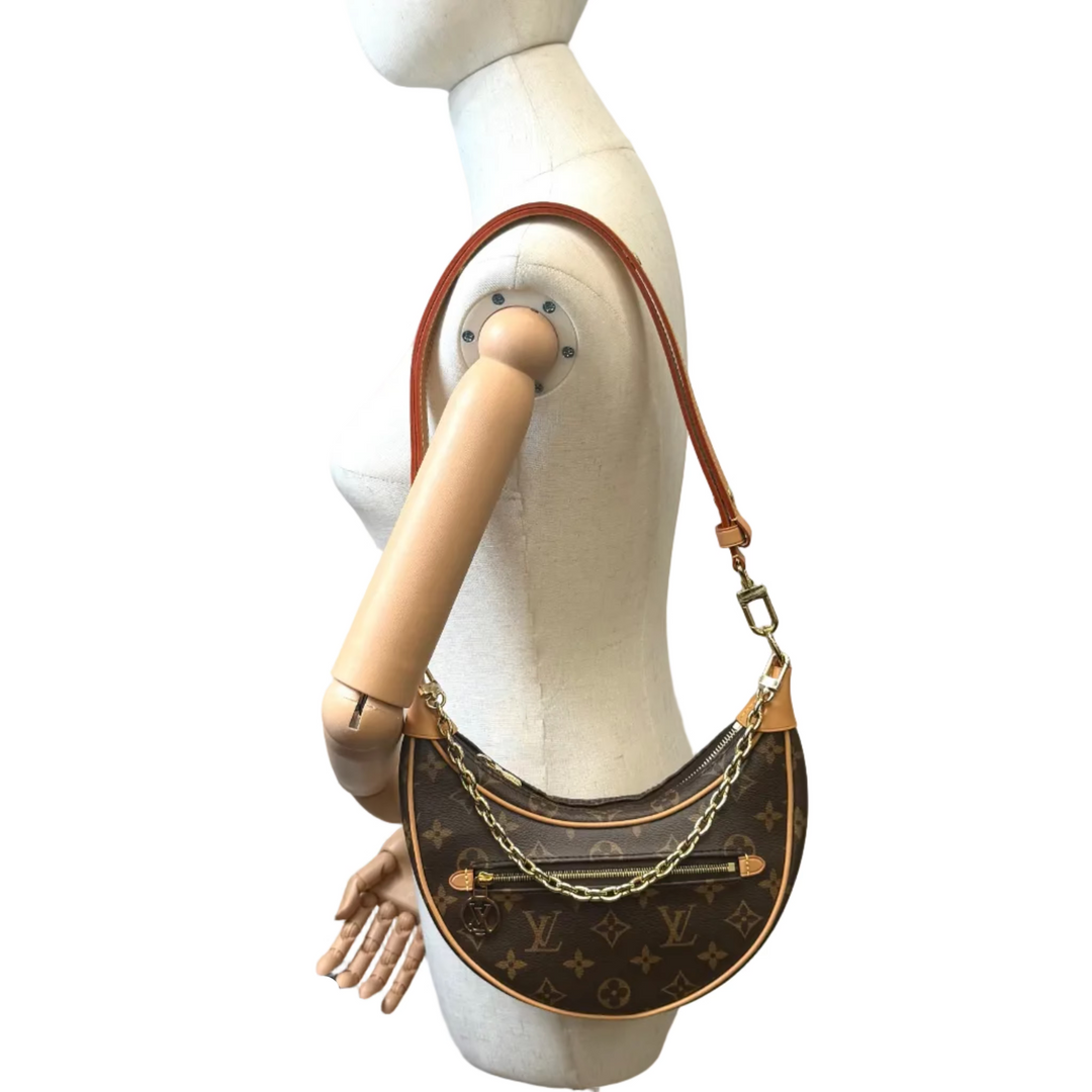 Louis Vuitton monogram canvas crescent shoulder bag with brown leather trim and chain strap, displayed on a cream-colored mannequin torso against a white background.