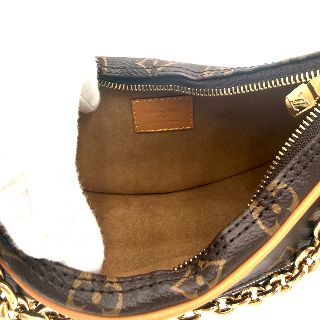 Close-up of the interior of a Louis Vuitton handbag, showing the brown monogram canvas exterior, tan leather interior lining, gold-tone zipper, and part of the gold chain strap.