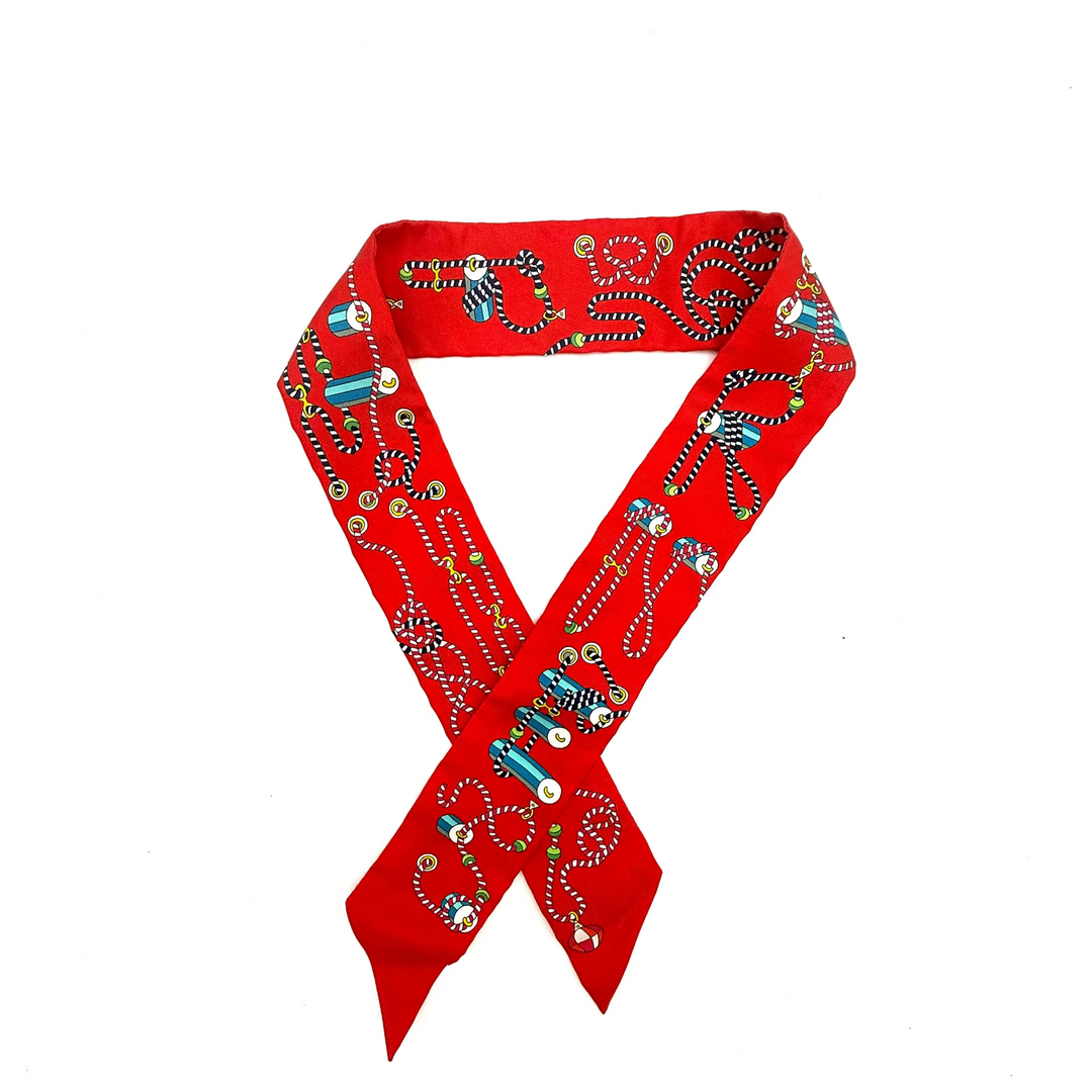 A red fabric scarf with intricate hand-embroidered patterns in blue, green, yellow, and white, arranged in a crossed loop on a plain white background.