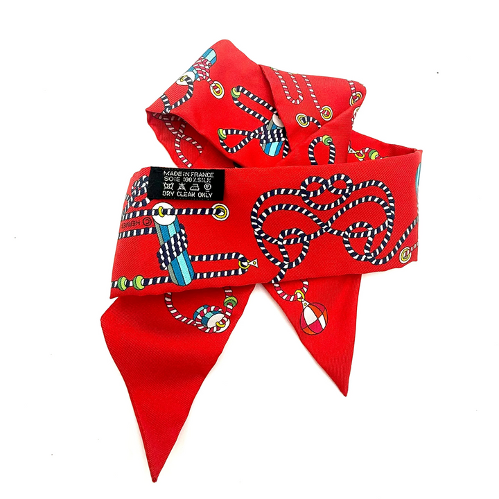 A red silk scarf with a black and white striped snake print, featuring a black neck label that reads 'MADE IN ITALY / SIZE 12 / SILK SCALPERS / FOR ELLONCE' and a small clear glass bead charm, photographed on a white background.