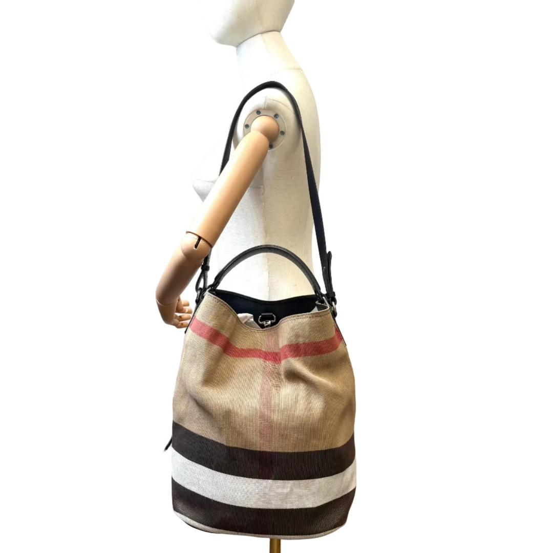 A beige bucket-style shoulder bag with black leather trim and a signature red and white stripe pattern, displayed on a wooden mannequin torso against a white background.