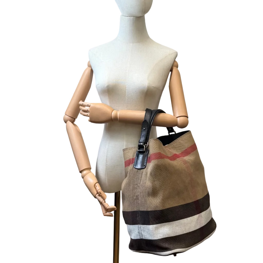 A vintage Burberry-style canvas tote bag with beige, brown, black, and red stripes, displayed on a wooden articulated mannequin torso against a white background.