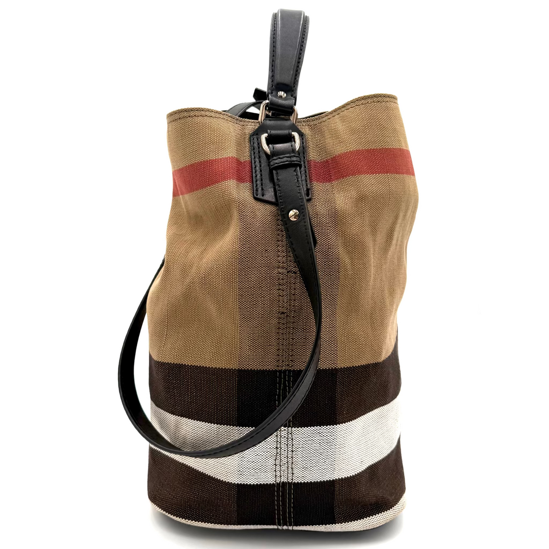 A vintage-style bucket bag made of canvas in beige, brown, and white with a red stripe, featuring a black leather top handle and shoulder strap.