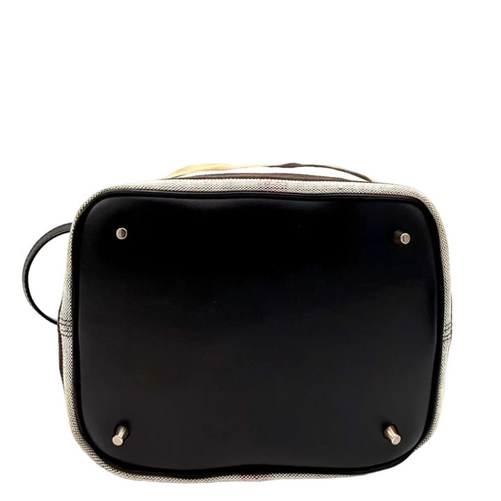 The bottom view of a black leather handbag with a beige and black plaid fabric trim, showing silver-toned metal studs and a black circular side loop on a white background.