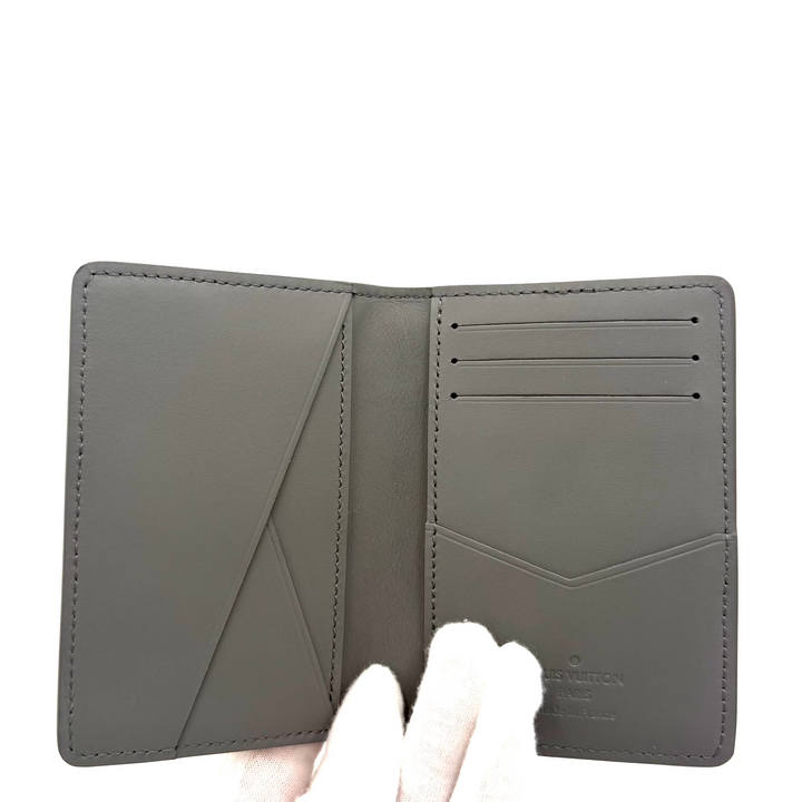 A dark gray leather bifold wallet held open by a white gloved hand, showing its interior card slots and geometric stitching details against a plain white background.