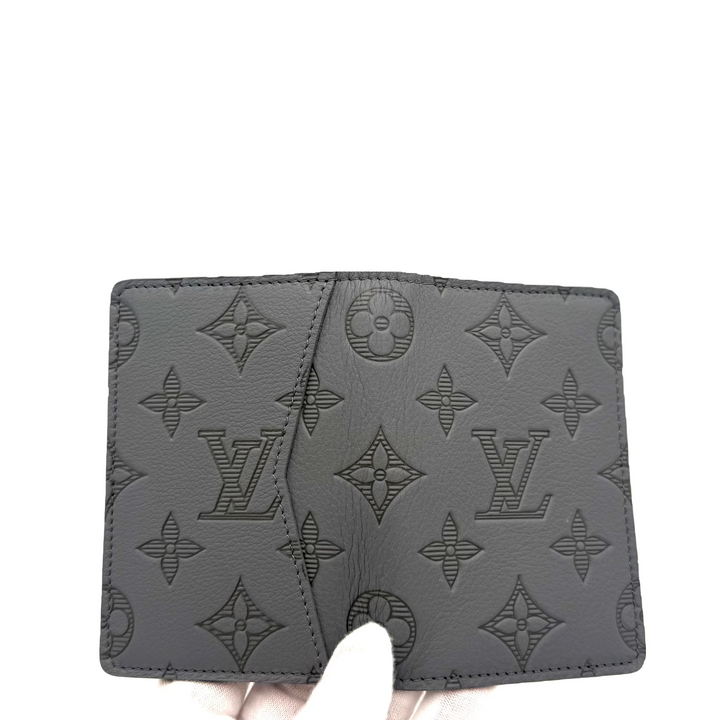 A dark gray Louis Vuitton monogram wallet held by a hand against a plain white background.