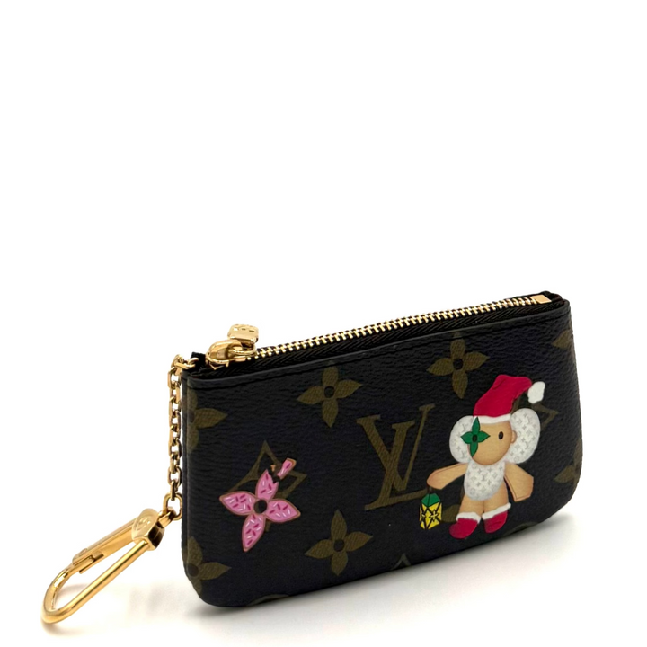 A small black Louis Vuitton monogram key pouch with a gold-tone zipper and chain, featuring a pink butterfly and a snowman wearing a Santa hat, set against a bright white background.
