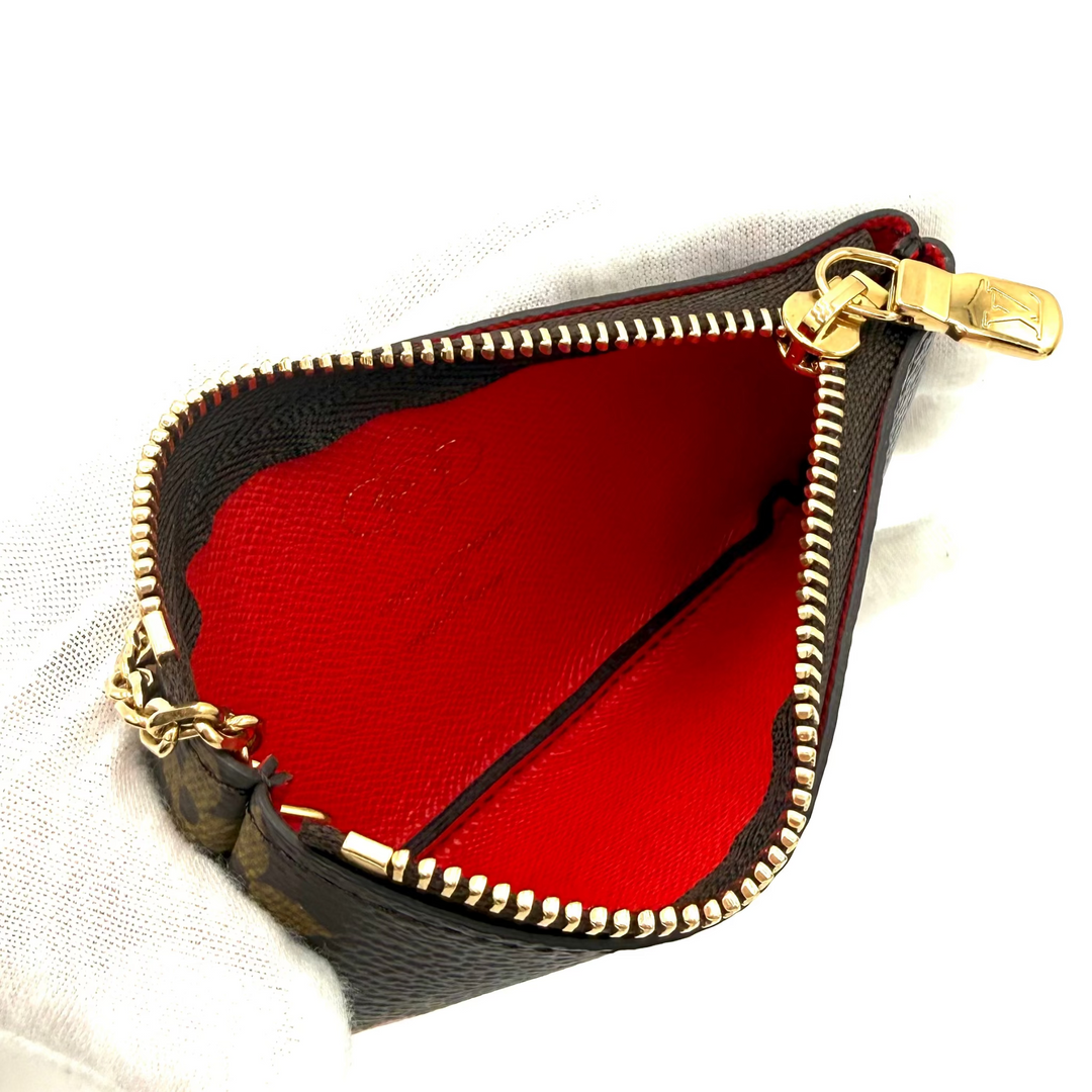 A small black leather coin purse with a bright red interior lining and gold-tone zipper, held by a white gloved hand against a white background.