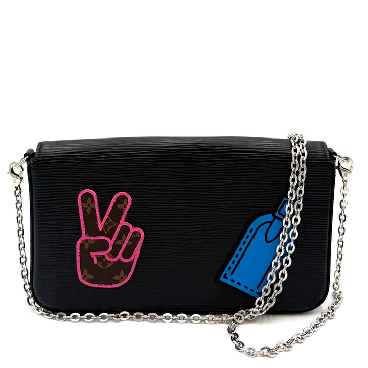 A black textured leather shoulder bag with a silver chain strap, featuring a pink peace sign patch and a blue price tag patch on the front.