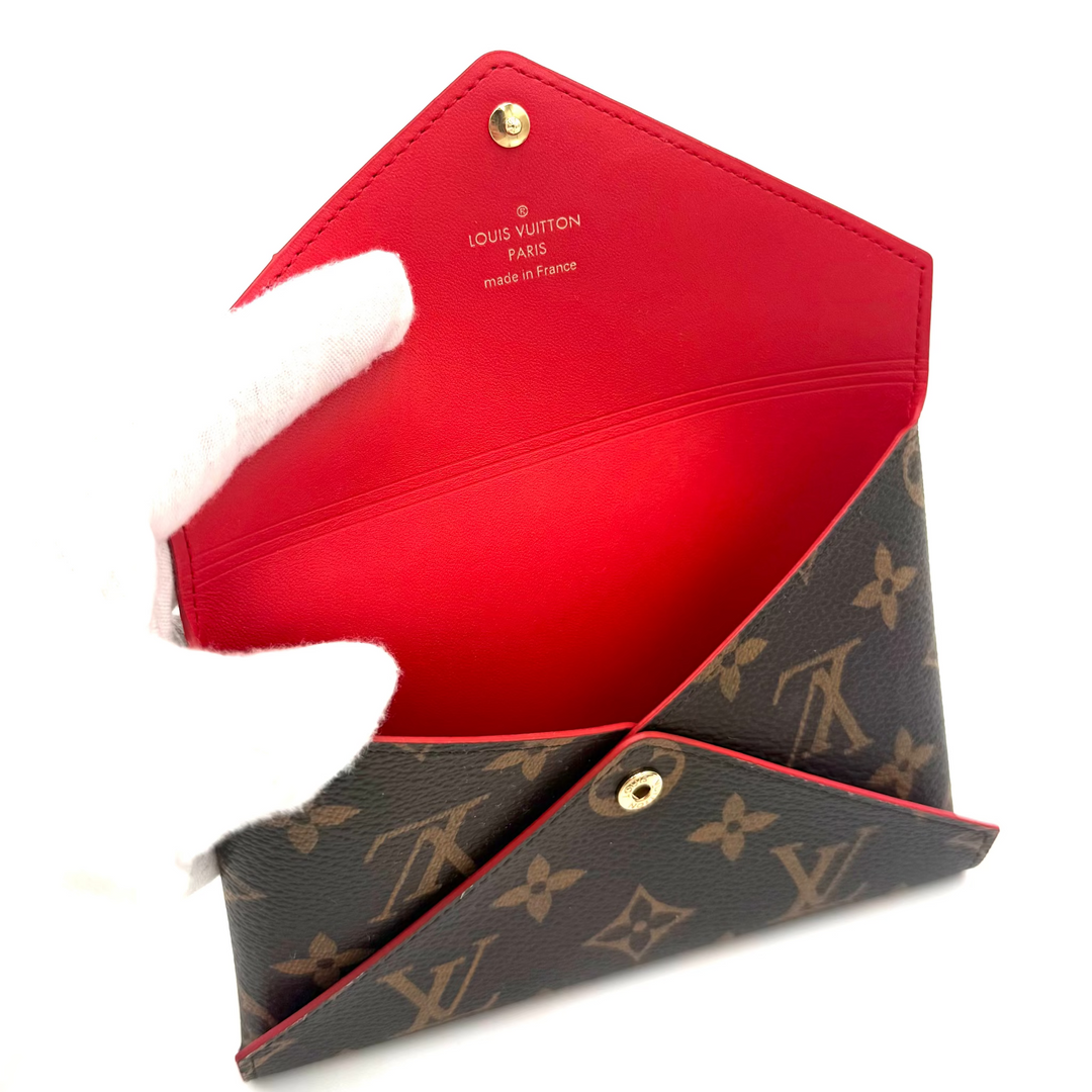 A Louis Vuitton monogram clutch bag shown open, featuring a dark brown coated canvas exterior with the classic tan LV monogram pattern and a vibrant red interior lining.
