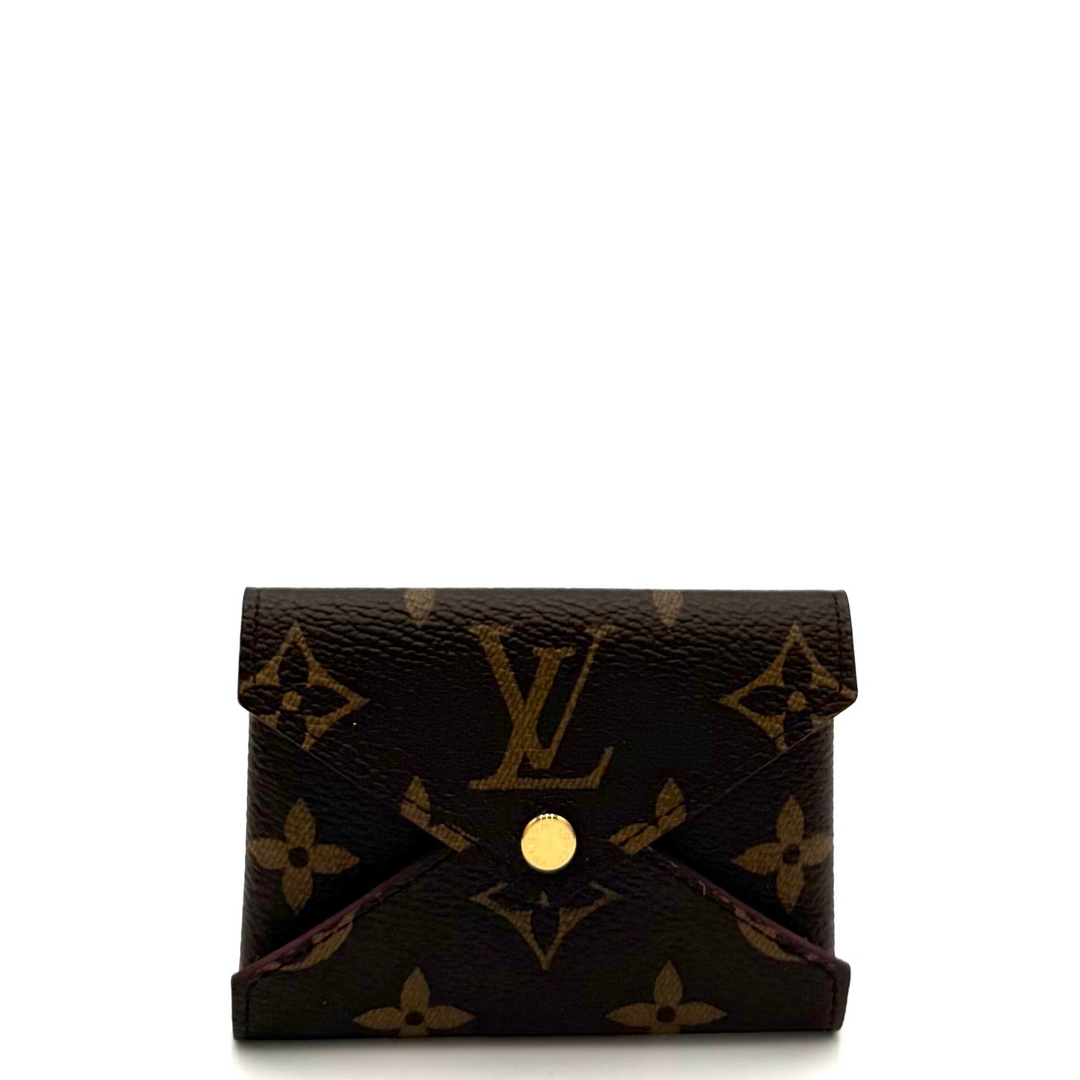 A small Louis Vuitton monogram wallet in dark brown coated canvas with gold-tone hardware, photographed on a plain white background with a studio reflector visible on the right side.