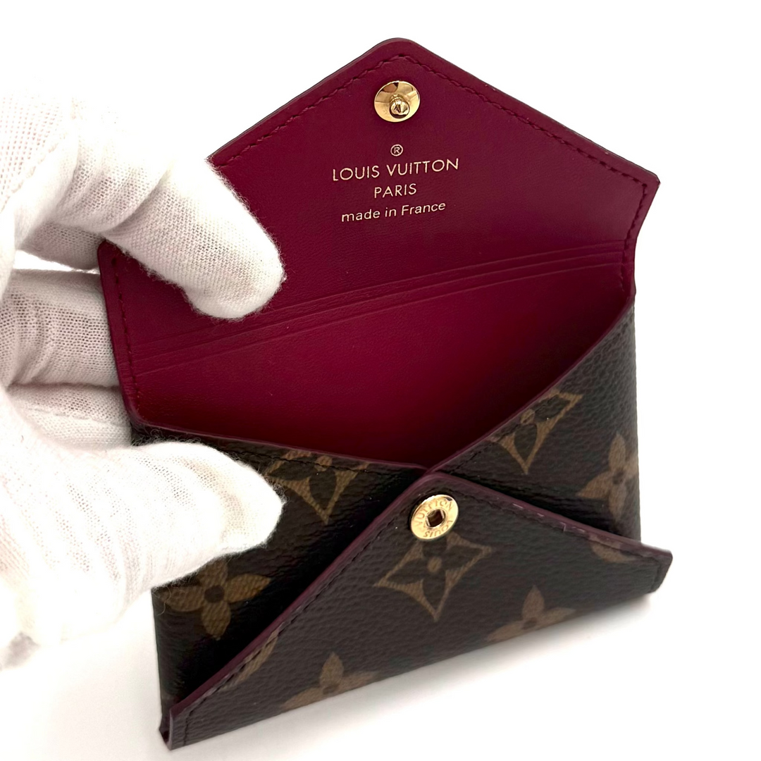 A Louis Vuitton monogram card holder wallet held open by a white gloved hand, showing a deep burgundy interior and gold-tone hardware on a plain white background.