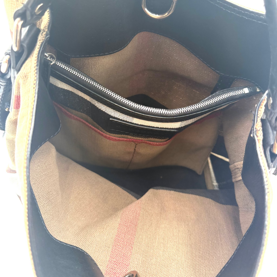 Close-up of the interior of a handbag, showing a beige and black fabric body, a black interior lining, a zippered pocket with a striped pattern, and a small red accent stripe.