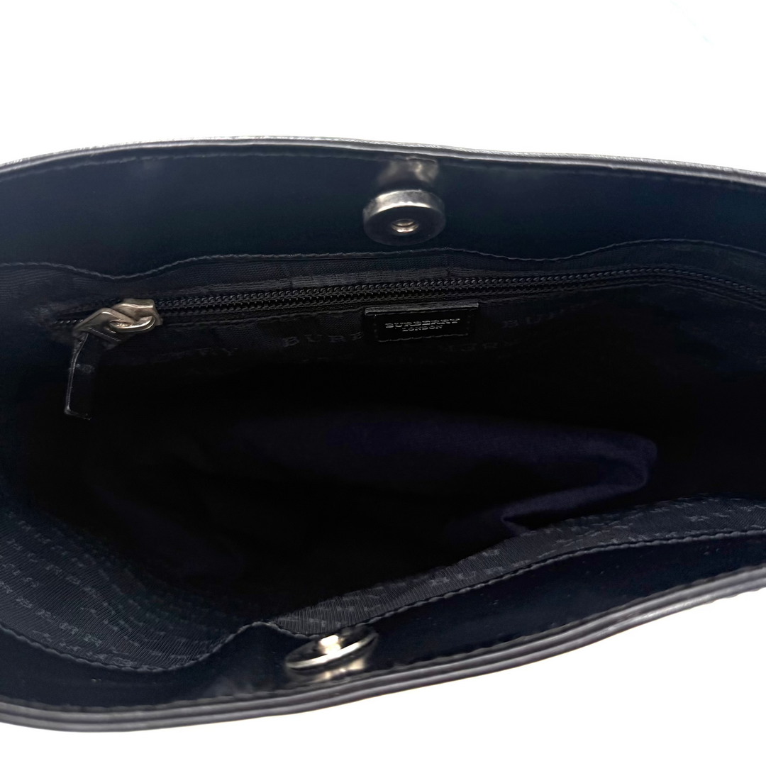 An open view of a black leather handbag showing its dark navy interior lining, a zippered pocket, and a small black interior label.