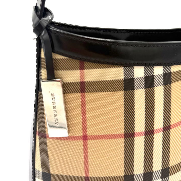 Close-up of a Burberry handbag showing the signature beige plaid pattern with black, brown, and red lines, a black leather trim and strap, and a silver-tone metal brand tag.