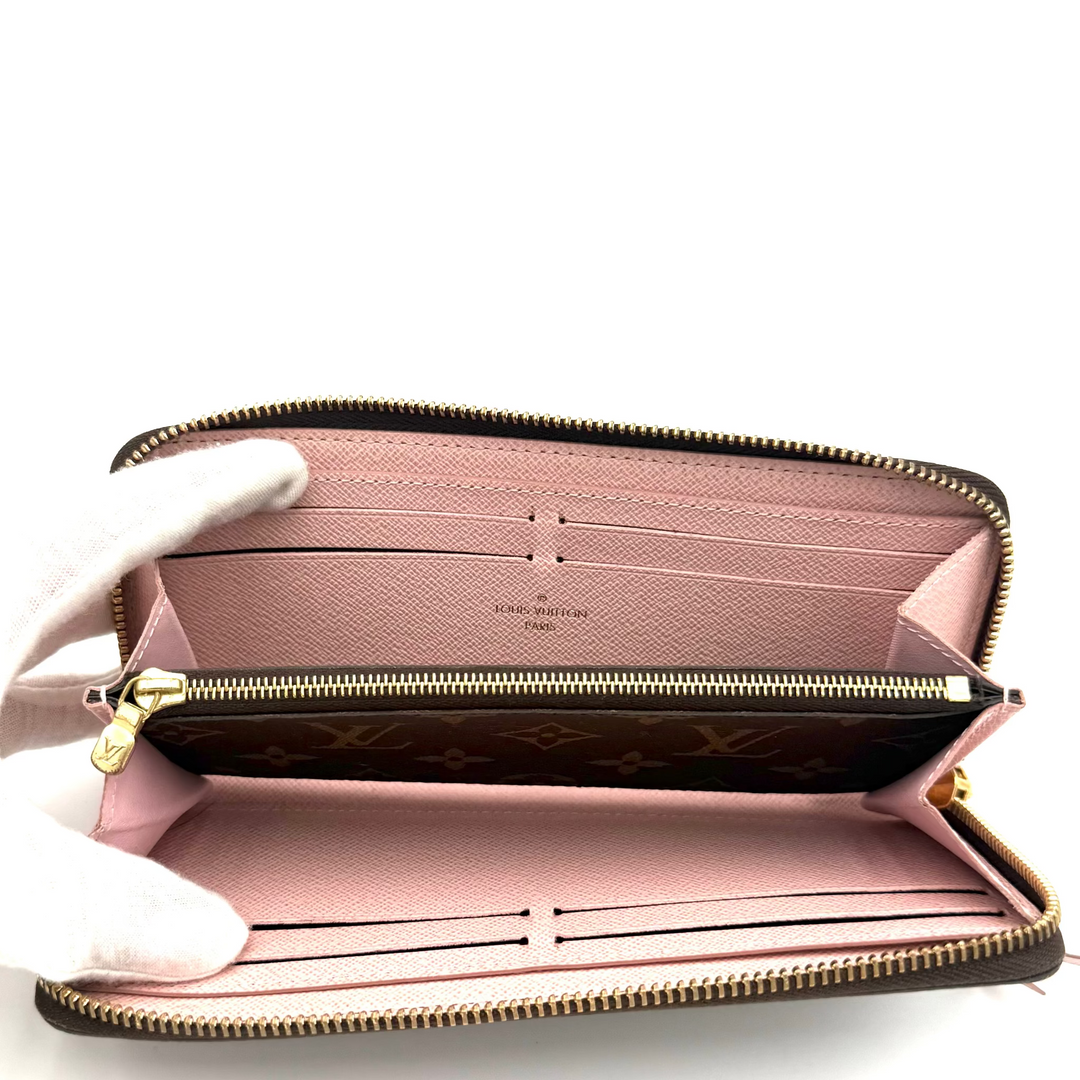 An open Louis Vuitton monogram zip-around wallet with a pink interior, held by a white-gloved hand against a white background.