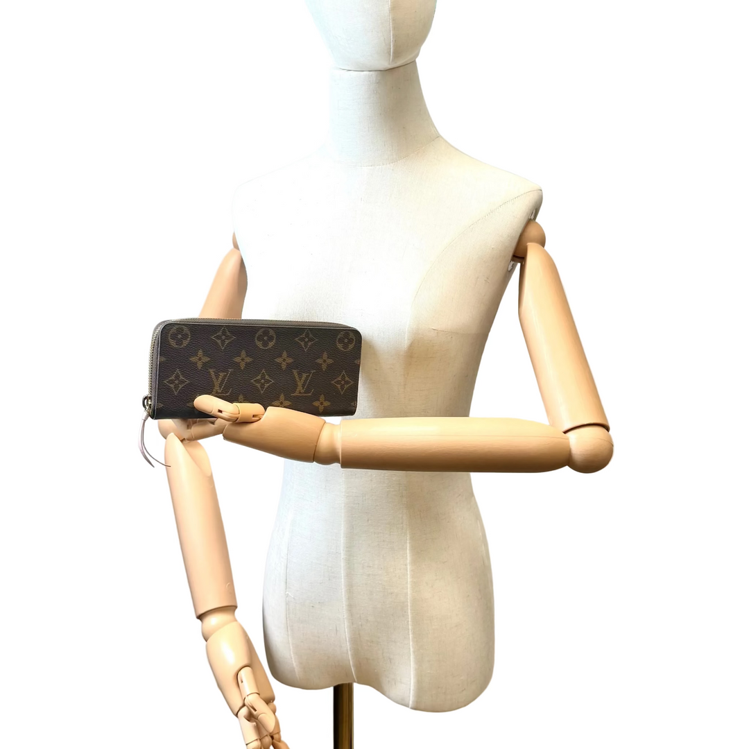 A Louis Vuitton monogram wallet or clutch held by a beige fabric dress form mannequin with wooden arms, set against an indoor wall background.