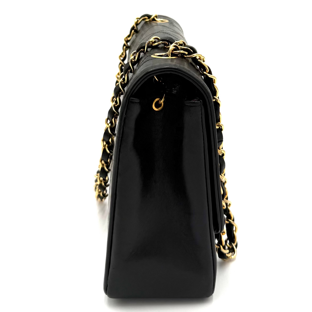 A black leather shoulder bag with a glossy finish, featuring a gold-tone chain strap woven with black leather and gold-tone metal links, shown from a side profile view on a white background.
