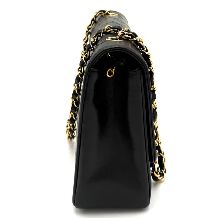 A black leather shoulder bag with a glossy finish, featuring a gold-tone chain strap woven with black leather and gold-tone metal links, shown from a side profile view on a white background.