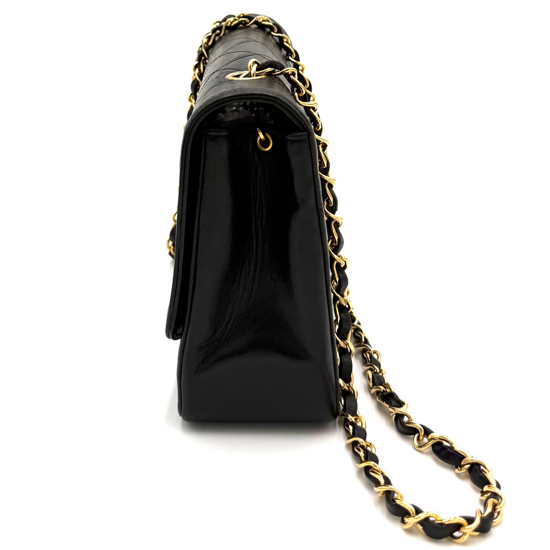 A black leather shoulder bag with a gold chain strap, shown from a side profile view on a white background.
