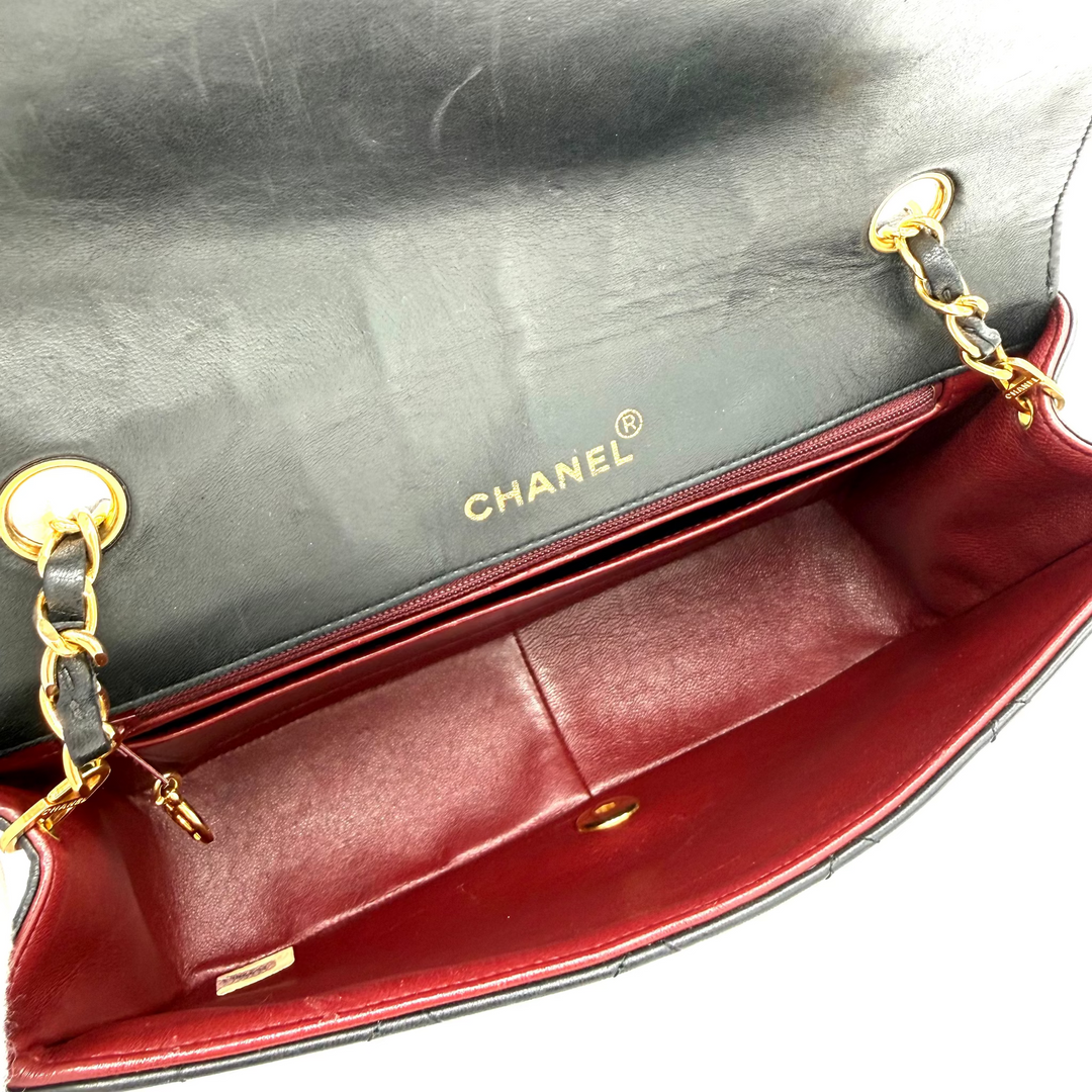 Close-up of a Chanel handbag interior showing a black leather exterior with gold hardware and a deep red leather lining. The word CHANEL is printed in gold on the inside flap.