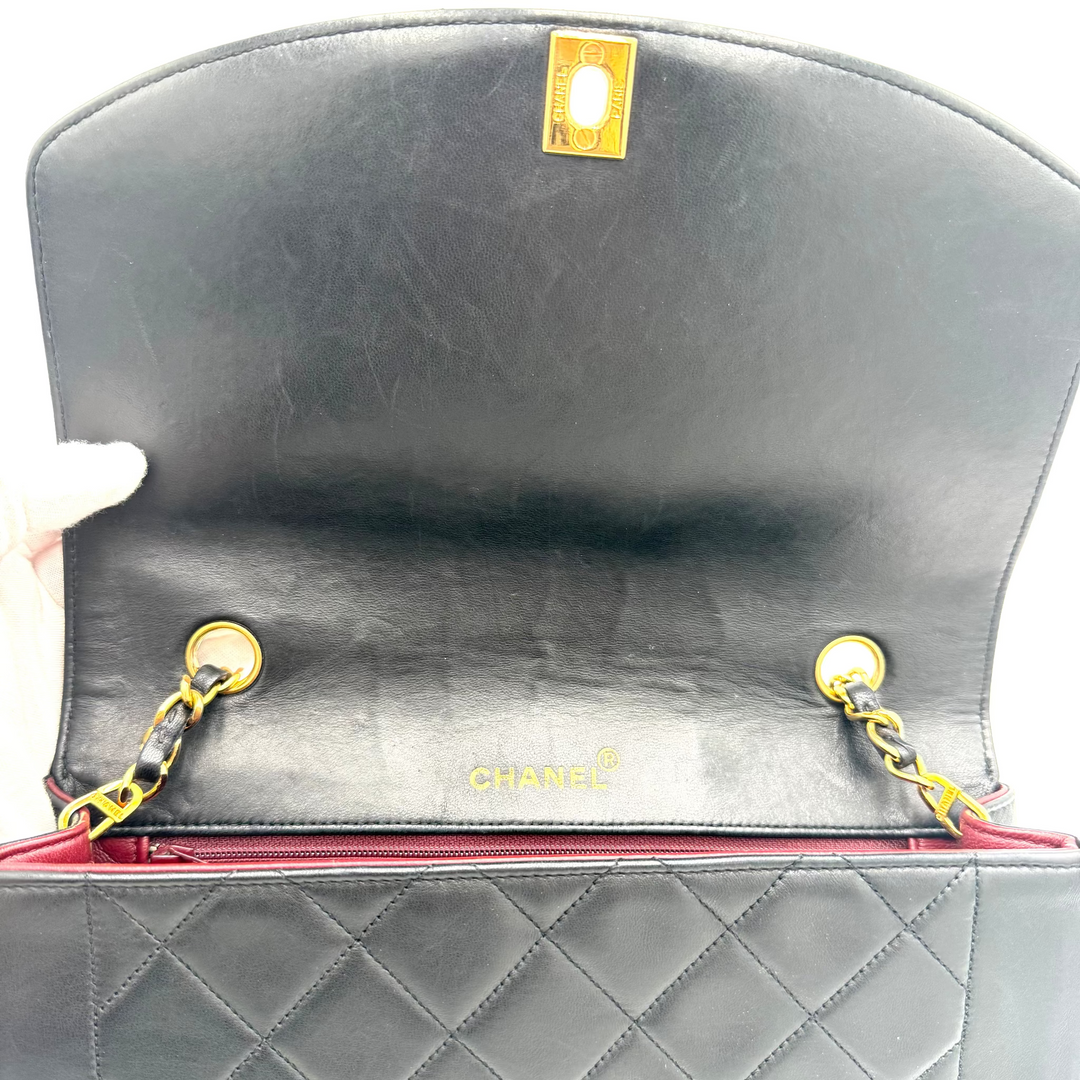 Close-up of a black quilted leather Chanel shoulder bag, showing the interior flap with gold-tone hardware, a gold CHANEL logo, and a red interior lining.