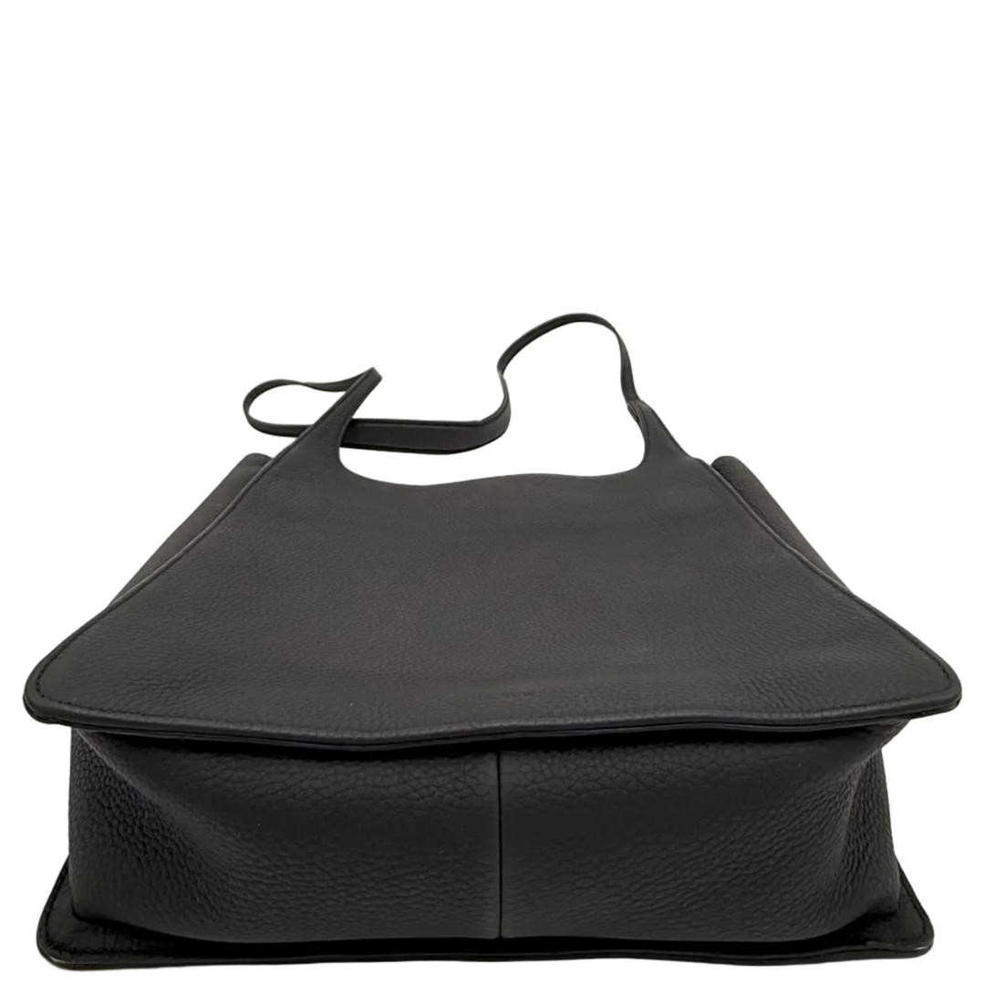 A black pebbled leather tote bag with a top handle, photographed from the front inside a white studio lightbox setup.