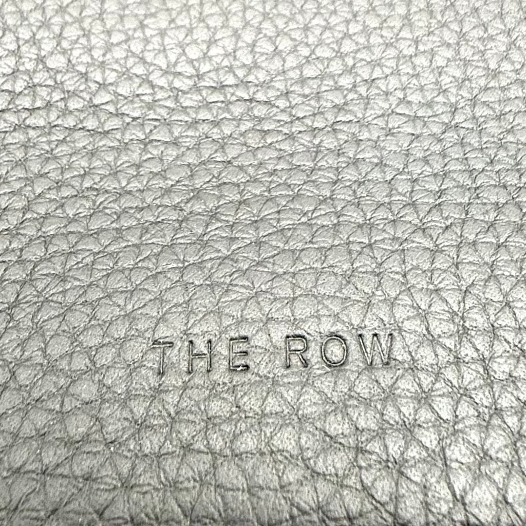 A close-up of a light gray pebbled leather handbag by The Row, showing the textured leather surface and a portion of the strap against a white background.