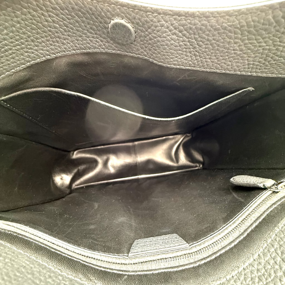 Close-up of the interior of a gray pebbled leather handbag, showing a black interior lining, a zippered compartment, and a small circular snap detail.