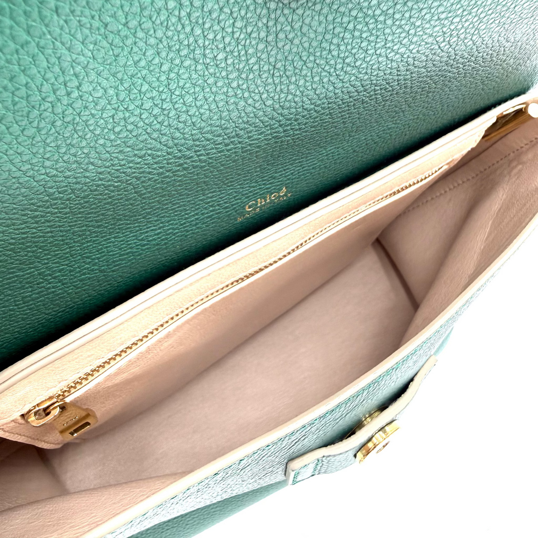 Close-up of a teal green pebbled leather handbag interior showing a gold-tone snap button, zipper, and beige lining.